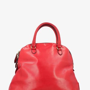 Op de afbeelding: Een felrode, koepelvormige handtas met een handvat aan de bovenkant en een ritssluiting. De tas heeft goudkleurige hardware en een gladde, glanzende afwerking. Een klassieke stijl.