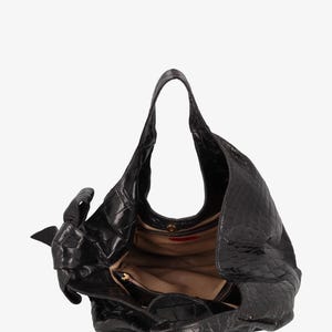 May include: Black leather handbag with a textured, crocodile-like pattern. The bag has a single shoulder strap and a large, open interior. A small, zippered pocket is visible inside. The bag is open, revealing a tan lining.