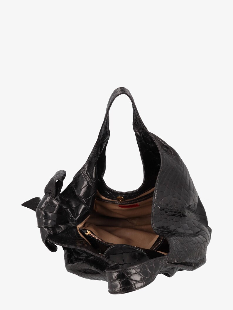 May include: Black leather handbag with a textured, crocodile-like pattern. The bag has a single shoulder strap and a large, open interior. A small, zippered pocket is visible inside. The bag is open, revealing a tan lining.