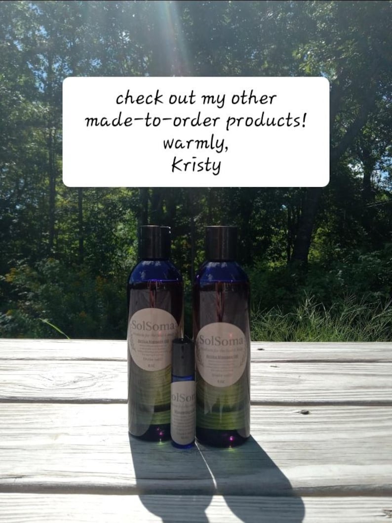 May include: Two dark blue bottles and a small roller bottle of SolSoma brand oil are displayed on a wooden surface. The bottles have white labels with text. A sign above reads "check out my other made-to-order products! warmly, Kristy."