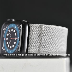 May include: A black Apple Watch with a gray sport band. The watch face is a blue and black analog clock with the text "COOL-DUA LIPA" on the bottom. The text "Available in a range of sizes to provide an ultracomfortable fit" is below the watch.