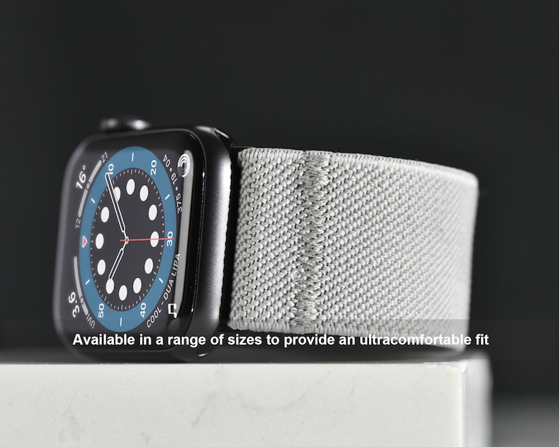 May include: A black Apple Watch with a gray sport band. The watch face is a blue and black analog clock with the text "COOL-DUA LIPA" on the bottom. The text "Available in a range of sizes to provide an ultracomfortable fit" is below the watch.