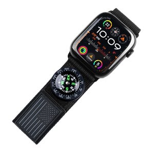Könnte beinhalten: Schwarze Smartwatch mit schwarzem Nylonarmband und eingebautem Kompass. Das Zifferblatt zeigt Uhrzeit, Datum und weitere Informationen an. Das Armband hat ein amerikanisches Flaggenmuster.