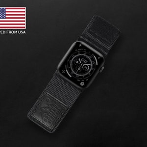 Puede incluir: Reloj Apple negro con una correa de nailon negra que presenta una esfera de reloj con brújula y cronógrafo. La correa tiene un parche de cuero negro con las palabras "FOR ALL YOUR ADVENTURES" grabadas en relieve.