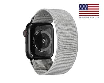 Puede incluir: Un Apple Watch Series 6 negro con una banda deportiva de bucle gris. La esfera del reloj es negra con texto blanco que dice "WATCH - SERIES 6 - APPLE - WR-50M -  ION-X GLASS -  APPLE WATCH"
