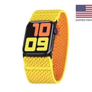 May include: A yellow and orange Apple Watch band with a black Apple Watch face displaying the time 10:09. The band is made of a woven material with a textured pattern.