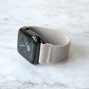 May include: A black Apple Watch with a gray elastic band. The watch face displays the time, date, and battery percentage.
