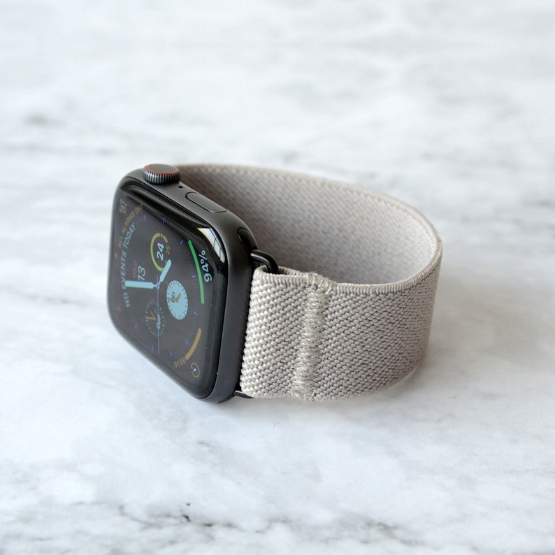 May include: A black Apple Watch with a gray elastic band. The watch face displays the time, date, and battery percentage.