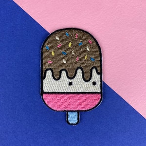 以下が含まれることがあります： カラフルなスプリンクルが散りばめられた、茶色とピンクの刺繍されたアイスクリームのポップシクルパッチ。ポップシクルは白い真ん中部分と青い棒を持っています。