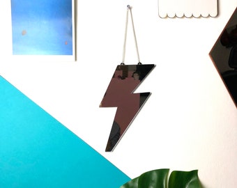 May include: A silver lightning bolt shaped mirror hanging on a white wall with a blue and white background. The mirror is reflecting the surrounding area.
