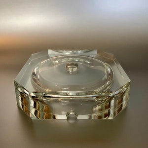 May include: A clear glass octagonal base with a round center hole. The base is designed to hold a candle or other decorative object.