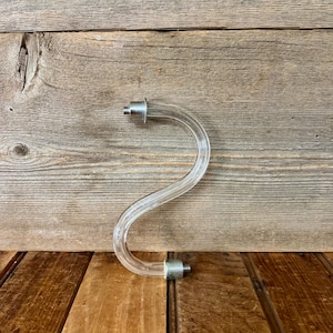 May include: A clear, S-shaped acrylic rod featuring a metallic silver-toned connector at each end. The curved, transparent component has a smooth, cylindrical profile and is designed with threaded metal fittings on both terminals for attachment.