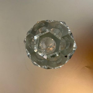 May include: A clear glass crystal knob with a hexagonal center and a faceted design.