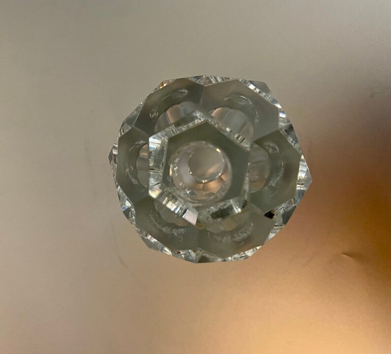 May include: A clear glass crystal knob with a hexagonal center and a faceted design.