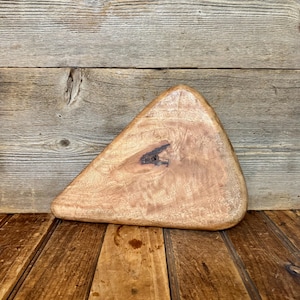 May include: A triangular wooden cutting board with a light brown finish and a prominent dark brown knot in the center. The board features a natural wood grain pattern with smooth, rounded edges and a thick, solid construction throughout.