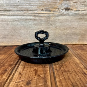 Puede incluir: Un porta anillos de vidrio negro con un asa decorativa. El porta anillos está sobre una superficie de madera.