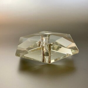 May include: A clear glass bottle stopper with a hexagonal base and a cylindrical top.