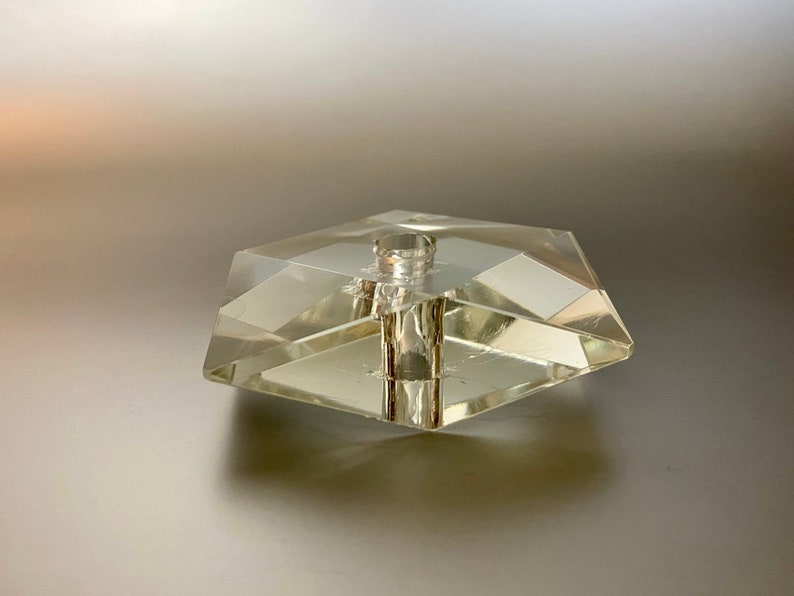 May include: A clear glass bottle stopper with a hexagonal base and a cylindrical top.