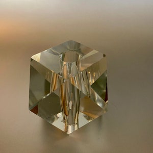 May include: A clear glass cube vase with a square opening at the top. The vase is made of faceted glass and has a geometric design.