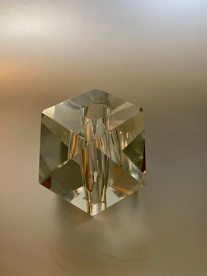 May include: A clear glass cube vase with a square opening at the top. The vase is made of faceted glass and has a geometric design.