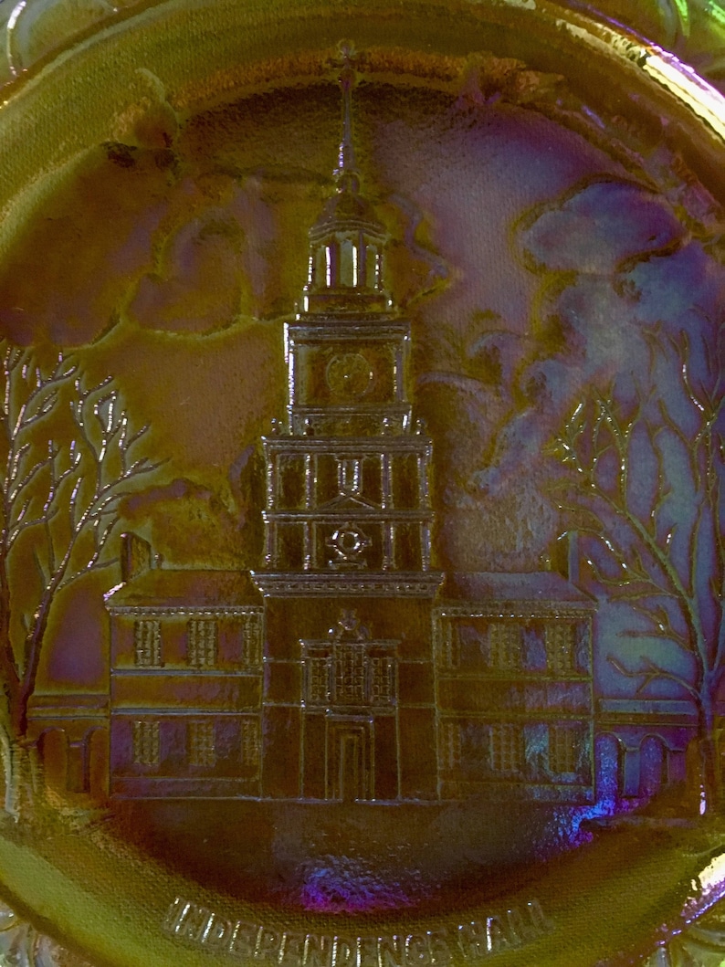 Peut inclure: Une assiette en verre iris&eacute; vintage avec une image en relief de l'Independence Hall &agrave; Philadelphie, en Pennsylvanie. L'assiette est de couleur dor&eacute;e avec une l&eacute;g&egrave;re teinte violette.
