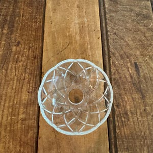 May include: A clear glass bowl with a decorative, geometric pattern. The bowl has a circular shape with a central hole and a scalloped edge. The bowl is likely for decorative purposes.