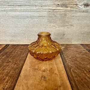 May include: Amber-colored glass decorative vase with a textured, bubble-like design. The vase has a round base and a flared top. The glass has a warm, golden hue, and the surface is covered in small, raised bumps.