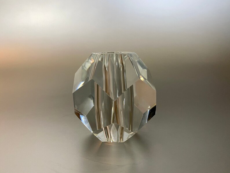 May include: A clear glass bead with a faceted design. The bead is round and has a smooth, polished surface.