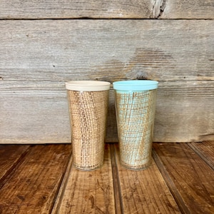 May include: Two clear glass tumblers with a burlap-like texture on the outside. One tumbler has a light blue rim and the other has a cream-coloured rim.