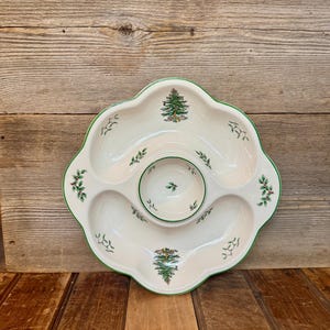 May include: White ceramic serving platter with a scalloped edge and a green trim. The platter has five sections, including a central dip bowl. Decorated with Christmas tree and holly designs.