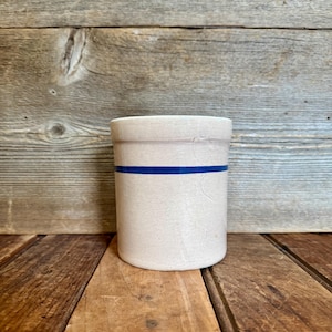 May include: A white ceramic mug with a black handle and the text "But First, Coffee" in a bold, black font. The mug is set against a blurred background, suggesting a cozy setting.