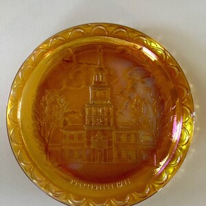 Peut inclure: Une assiette ronde en verre ambr&eacute; avec un bord festonn&eacute; sur&eacute;lev&eacute;. L'assiette pr&eacute;sente une image grav&eacute;e de l'Independence Hall &agrave; Philadelphie, en Pennsylvanie.