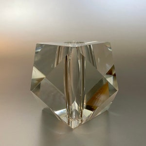 May include: A clear glass vase with a geometric shape. The vase has a square base and a rectangular opening at the top.