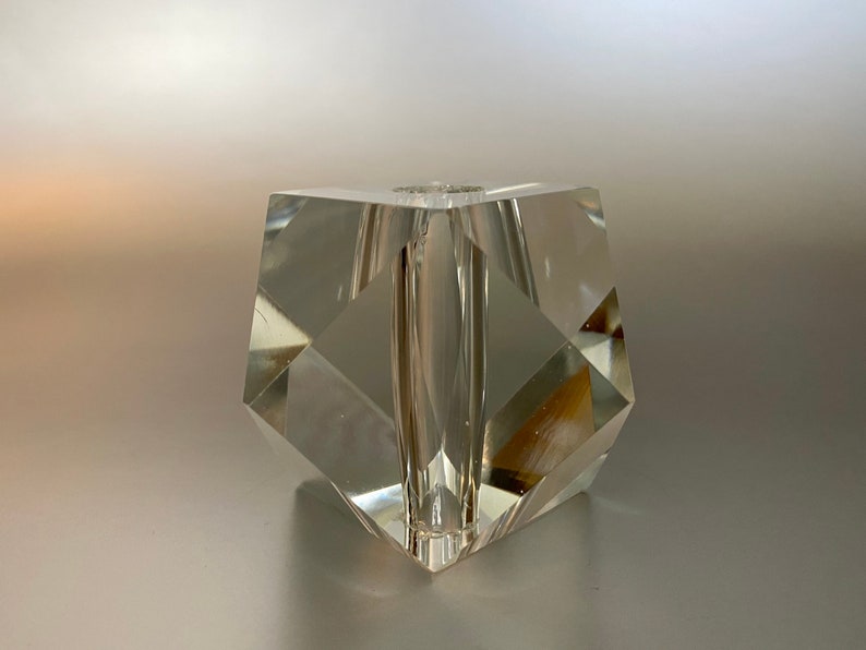 May include: A clear glass vase with a geometric shape. The vase has a square base and a rectangular opening at the top.