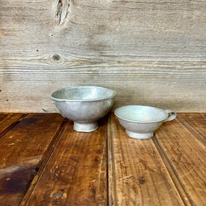 May include: Two silver metal funnels of different sizes, sitting on a wooden surface.