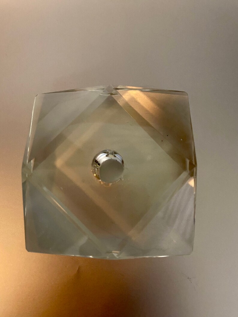 May include: A clear glass crystal prism with a faceted design and a hole in the center. The prism is a light beige color.