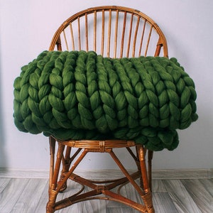 May include: A dark green chunky knit throw blanket draped over a wicker chair. The chair has a rounded back and a woven seat.