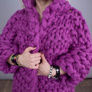 K&ouml;nnte beinhalten: Ein &uuml;bergro&szlig;er, grob gestrickter Cardigan in Magenta mit Kapuze. Die dicke, handgestrickte Textur ist der Blickfang. Der Cardigan ist ein auff&auml;lliges Mode-Statement, ideal f&uuml;r W&auml;rme und Stil. Die &Auml;rmel sind lang und die Passform ist locker.