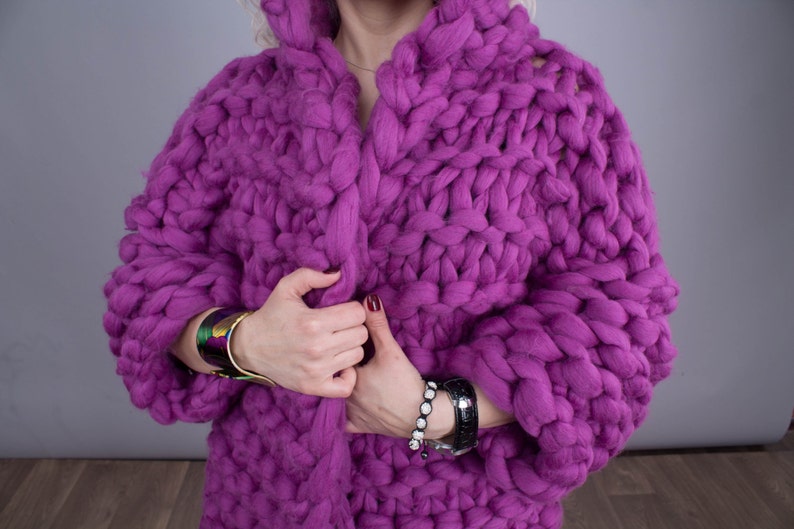 K&ouml;nnte beinhalten: Ein &uuml;bergro&szlig;er, grob gestrickter Cardigan in Magenta mit Kapuze. Die dicke, handgestrickte Textur ist der Blickfang. Der Cardigan ist ein auff&auml;lliges Mode-Statement, ideal f&uuml;r W&auml;rme und Stil. Die &Auml;rmel sind lang und die Passform ist locker.