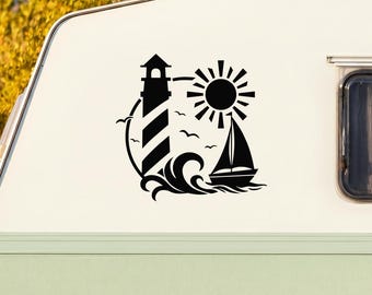 May include: A black vinyl decal applied to the side of a white camper, featuring a graphic design of a striped lighthouse, a sailboat on stylized waves, a sun with rays, and small birds flying in the background against the white surface.