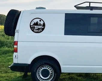 May include: White van with a black roof rack and a black and white "Van Life" decal on the side. The van is parked in a field of yellow flowers.
