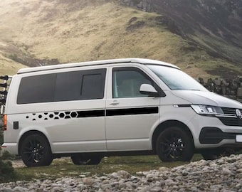 May include: A white Volkswagen van featuring a black horizontal side decal with a geometric honeycomb pattern. The vehicle is equipped with black wheels and a rear-mounted rack, showcasing a sleek exterior design for a modern camper van aesthetic.