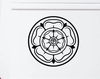 May include: A black circular decal featuring a stylized Tudor rose design with layered petals and a central bud, applied to the white rear panel of a van. The graphic consists of bold, clean lines forming a symmetrical floral emblem.