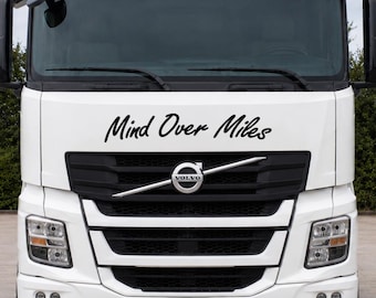 May include: A white Volvo semi-truck featuring a black grille with the Volvo logo and the text Mind Over Miles in black script lettering on the front panel. The truck has large side mirrors, a windshield, and headlights on the front bumper.