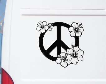 May include: A black vinyl decal featuring a central peace sign symbol surrounded by white hibiscus flowers with black outlines. The decal is applied to the white rear panel of a vehicle, displaying a high-contrast graphic design on a flat surface.
