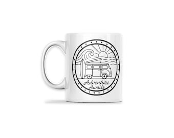 May include: A white ceramic mug featuring a black circular line art graphic. The design depicts a camper van with a surfboard, ocean waves, and a sun. The text Adventure Awaits is printed in a cursive script font inside the circle.