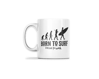 May include: A white ceramic mug featuring a black graphic of human evolution progressing from an ape to a surfer carrying a surfboard. Below the graphic, the text reads BORN TO SURF in bold capital letters and forced to work in smaller font.