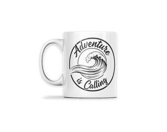 May include: A white ceramic mug featuring a black circular graphic on the front. Inside the circle is a detailed illustration of a crashing ocean wave. The text Adventure is Calling is printed in a black script font along the circular border.