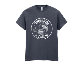 May include: A dark gray short-sleeve t-shirt featuring a white circular graphic on the chest. The design depicts a stylized ocean wave inside the circle with the text Adventure is Calling written in a white script font around the wave.