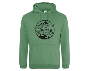 May include: A sage green hooded sweatshirt featuring a black circular graphic on the chest. The design includes a mountain range, pine trees, a winding road, and the text "ADVENTURE BEFORE DEMENTIA" printed in a bold, dark font.